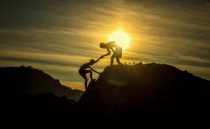 Deux silhouettes qui s'entraident sur une montagne en se donnant la main