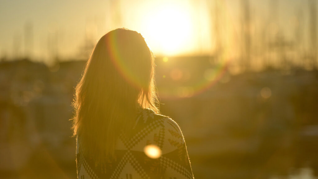 Femme de dos face au soleil couchant